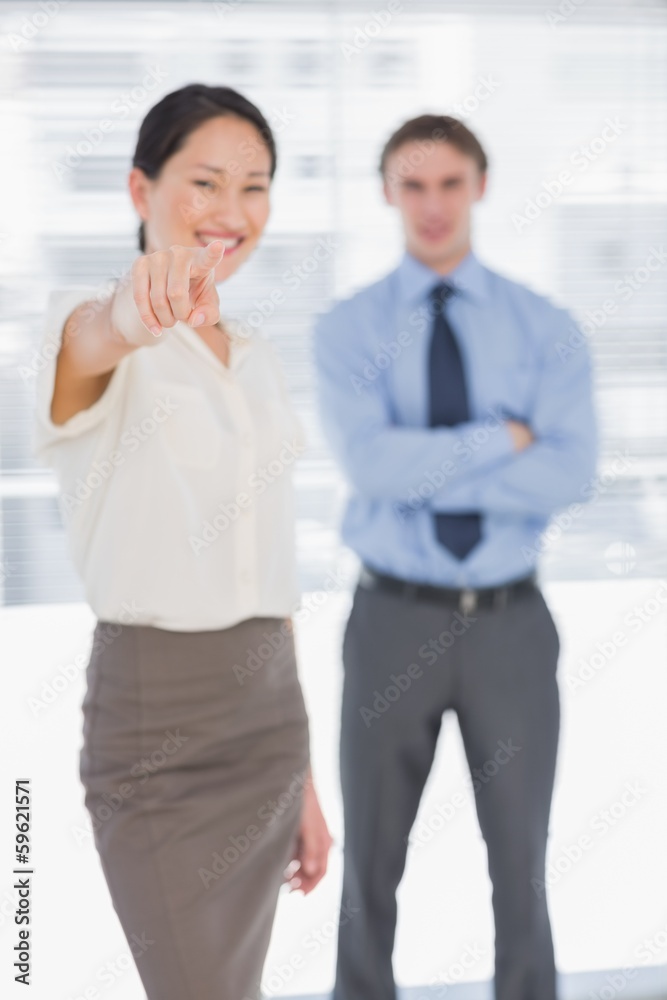 Businesswoman pointing towards the camera with man in office Businesswoman pointing towards the camera with man in office