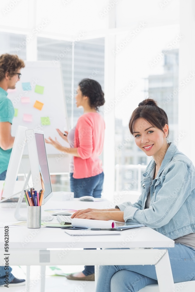 Casual woman using computer with colleagues behind in office Casual woman using computer with colleagues behind in office