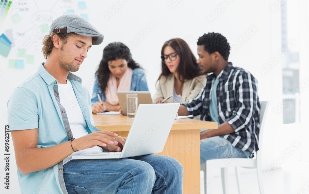 Casual man using laptop with colleagues behind in office Casual man using laptop with colleagues behind in office