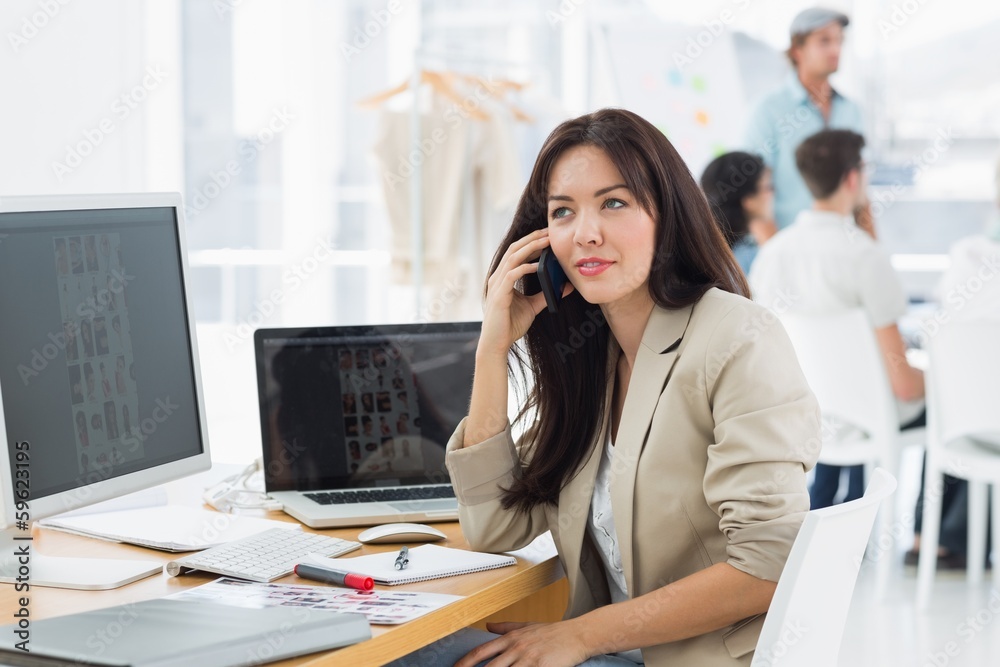 Woman on call at desk with colleagues behind in office Woman on call at desk with colleagues behind in office