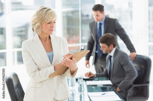 Businesswoman writing on clipboard with colleagues in background