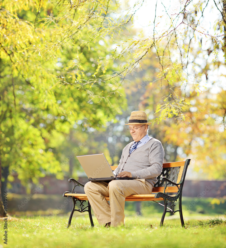 Senior man on bench and working on a laptop in a park Senior man on bench and working on a laptop in a park