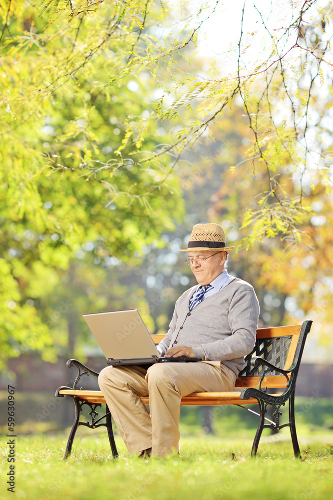 Senior man on a bench and working on a laptop in a park Senior man on a bench and working on a laptop in a park