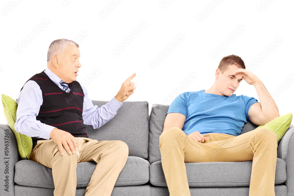 Father reprimending his son seated on a modern sofa Father reprimending his son seated on a modern sofa
