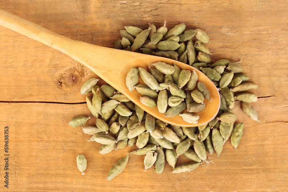 green cardamom in wooden spoon on wooden background close-up green cardamom in wooden spoon on wooden background close-up