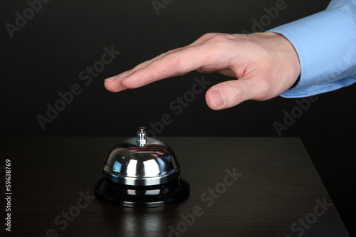 Hand ringing in service bell on wooden table on black