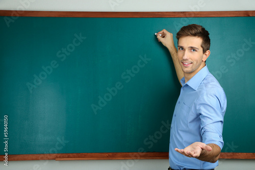 Young teacher near chalkboard in school classroom