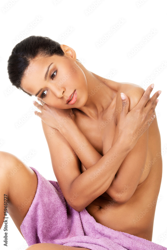 Attractive naked woman sitting covered with towel. Front view.