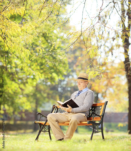 Senior man with hat sitting on a bench and reading a novel