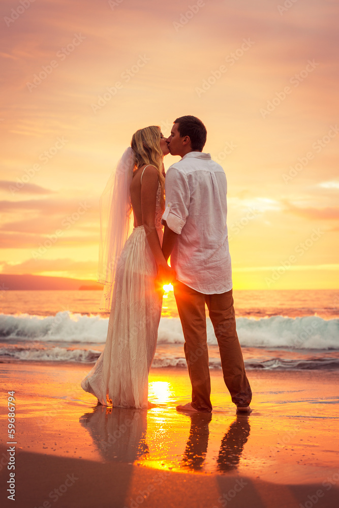 Just married couple kissing on tropical beach at sunset