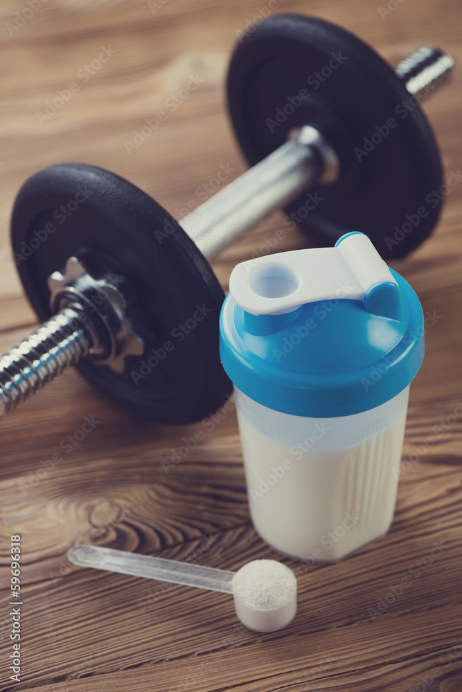 Protein shake and a dumbbell on a wooden surface Protein shake and a dumbbell on a wooden surface
