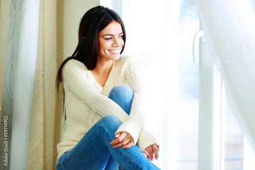 Young cheerful woman sitting on a window-sill