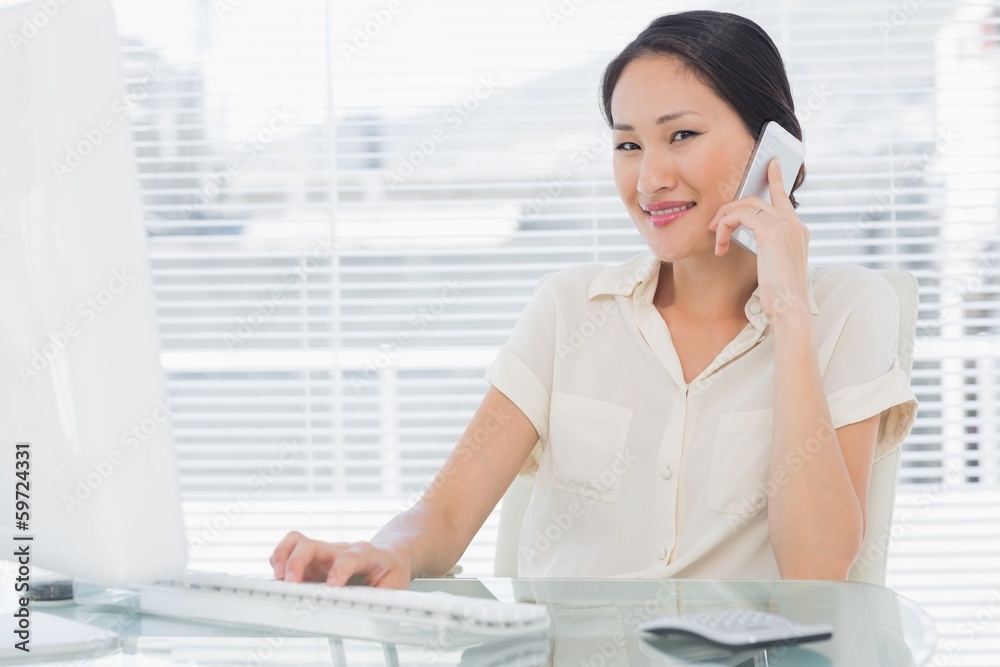 Businesswoman using cellphone and computer at desk Businesswoman using cellphone and computer at desk