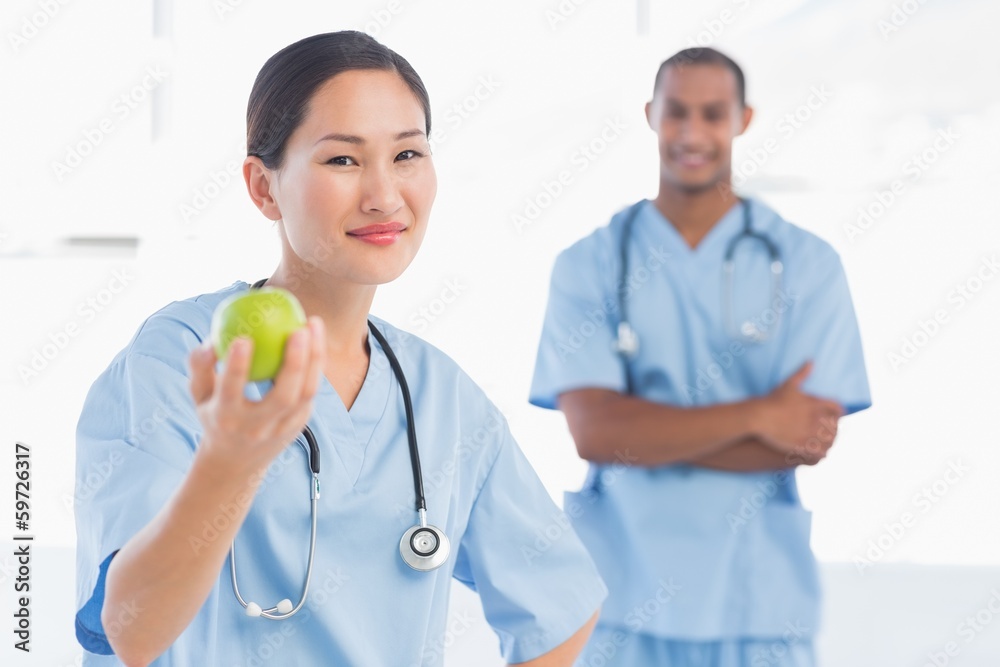Smiling surgeon holding an apple with colleague in hospital Smiling surgeon holding an apple with colleague in hospital