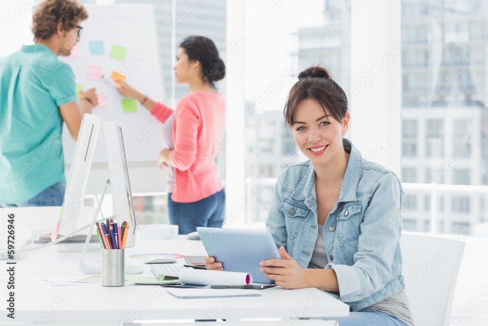 Casual woman using digital tablet with colleagues behind in offi Casual woman using digital tablet with colleagues behind in offi
