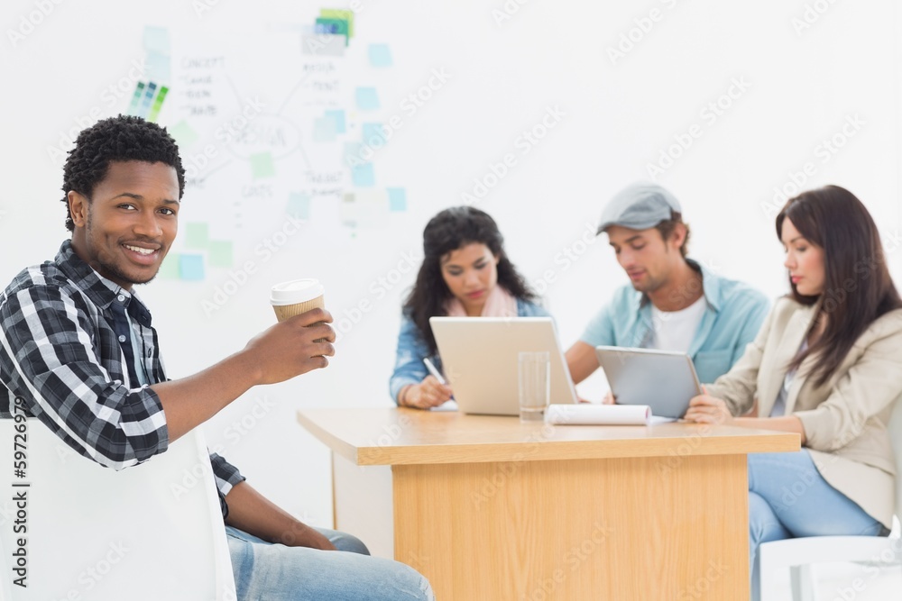Man holding take away coffee cup with colleagues behind Man holding take away coffee cup with colleagues behind