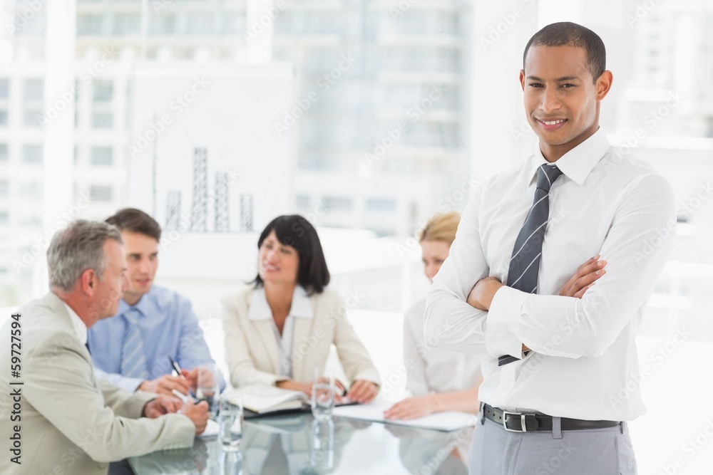 Fototapeta premium Young businessman looking at camera while staff discuss behind h