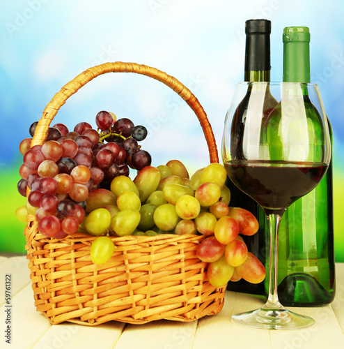 Ripe grapes in wicker basket, bottles and glass of wine,