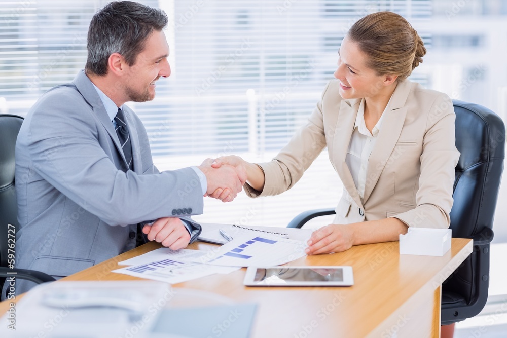 Colleagues shaking hands in a business meeting at office desk Colleagues shaking hands in a business meeting at office desk