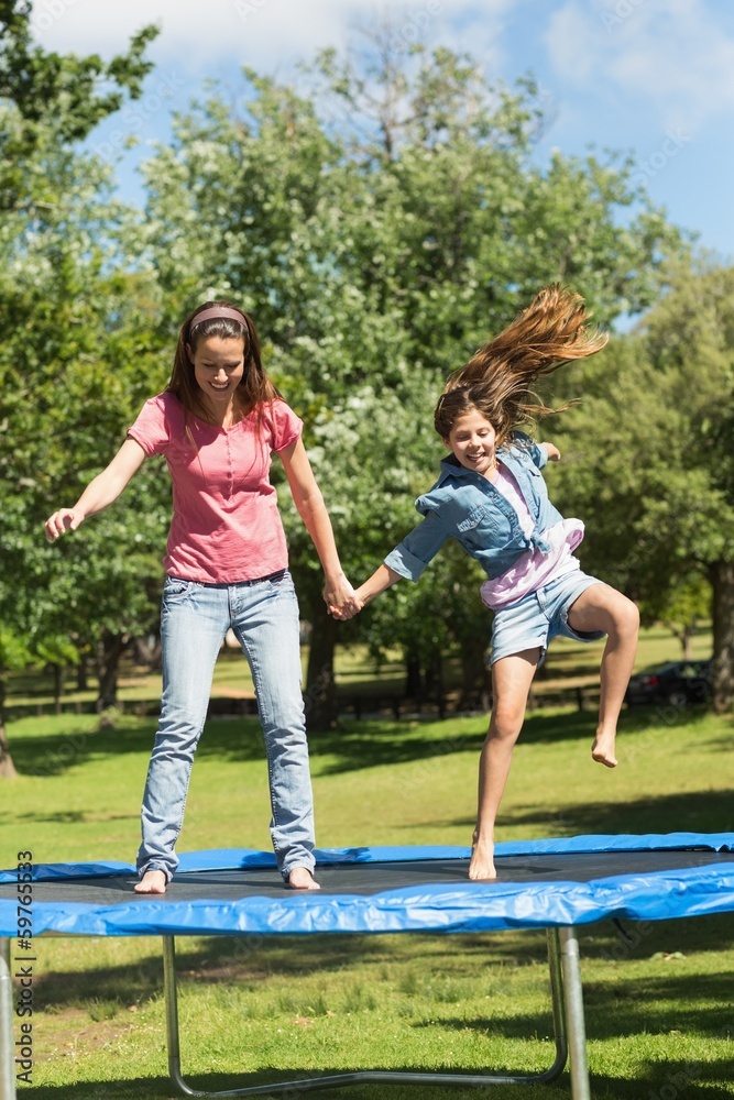 Fototapeta premium Happy girl and mother jumping high on trampoline in park