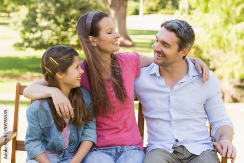 Smiling couple with daughter sitting on park bench