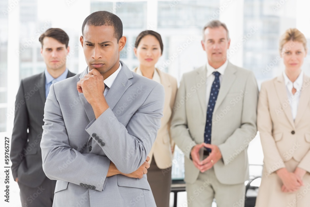 Serious businessman frowning at camera with team behind him Serious businessman frowning at camera with team behind him