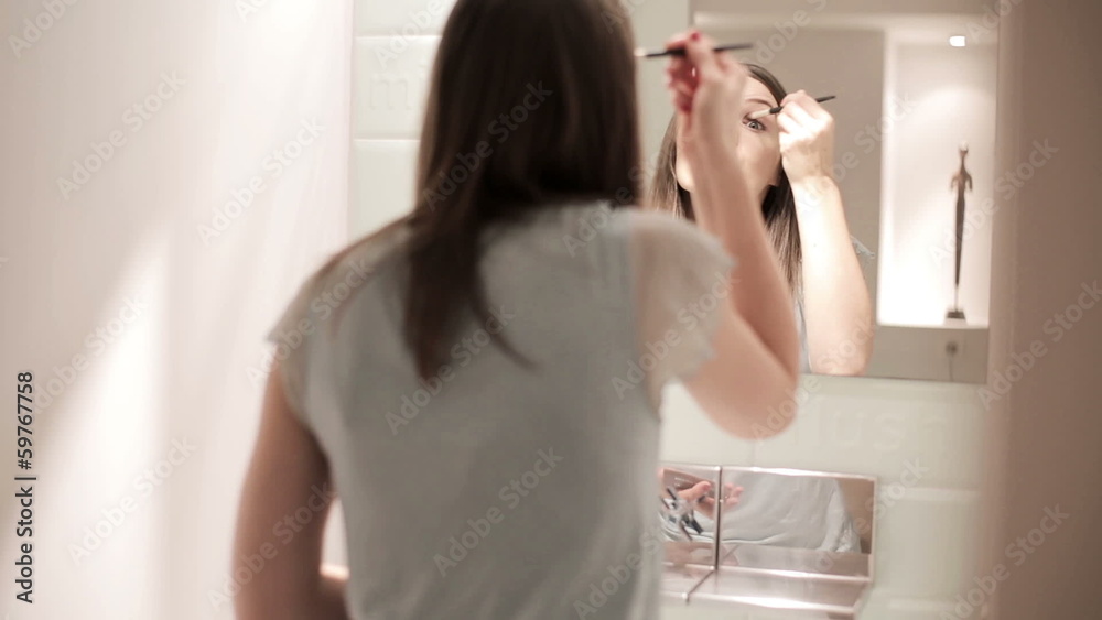 Young woman applying eyelid makeup in front of the mirror