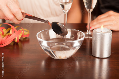 Damenhand hält Löffel über Wasser (Bleigießen)