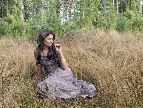 The woman in a sundress sits in not oblique grass