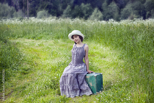 The girl  is sitting on a suitcase in the field