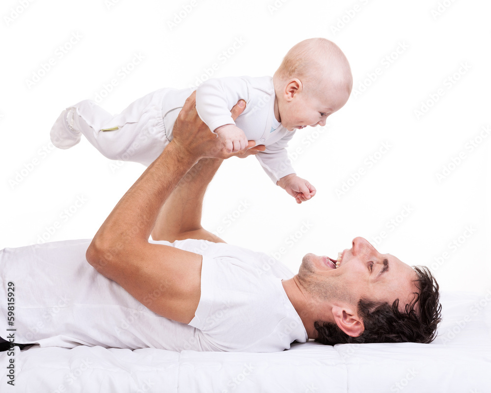 Happy young man holding baby son while lying on back Happy young man holding baby son while lying on back