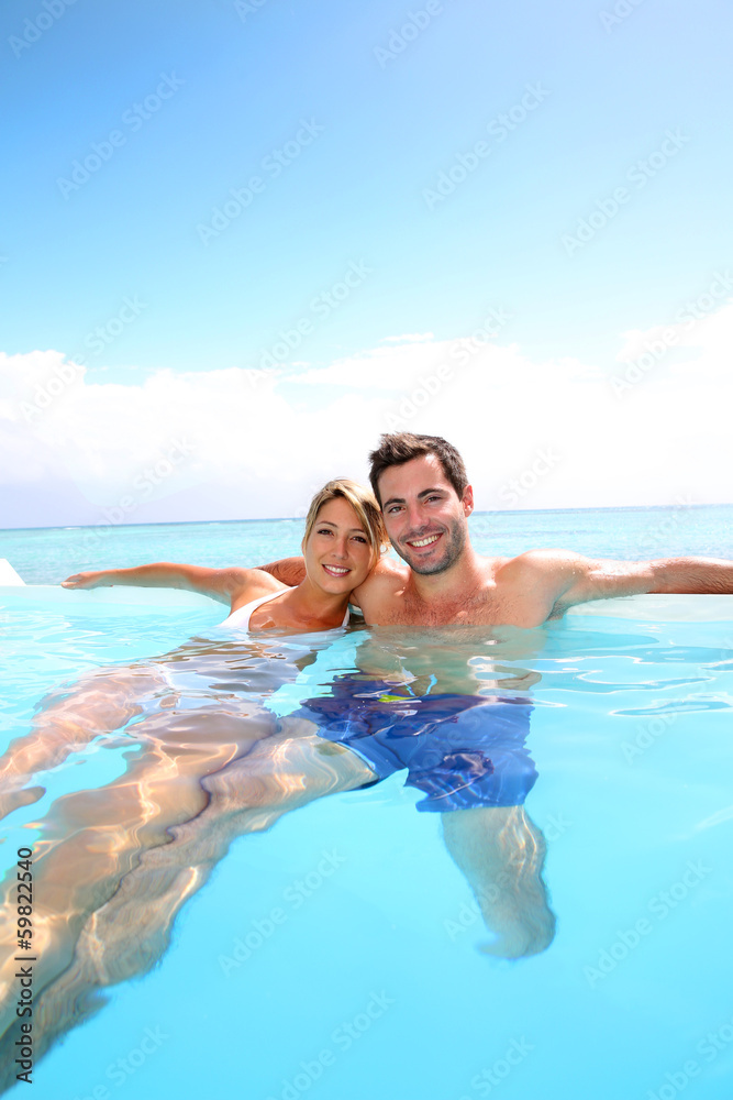 Cheerful couple swimming in infinity pool