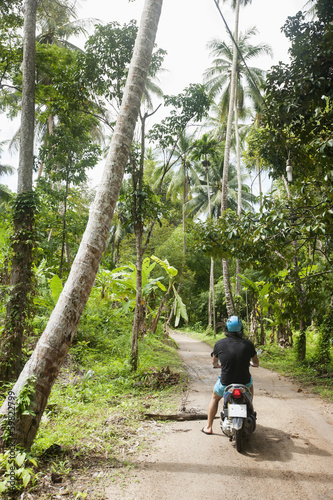Rear view of young man riding scooter on an unpaved road, Koh Pha Ngan, Thailand