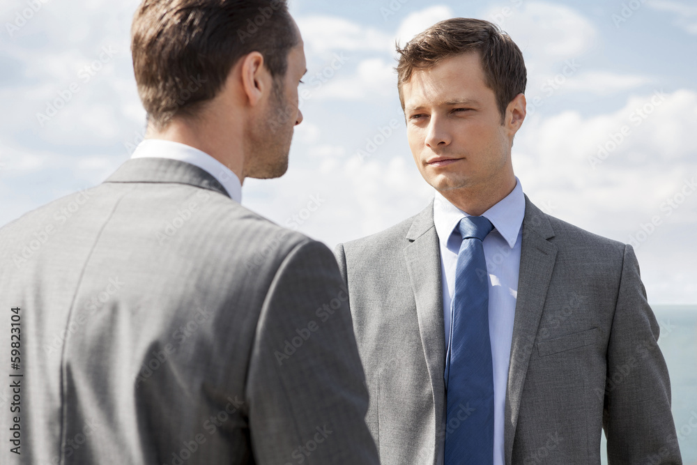 Businessmen looking at each other against sky Businessmen looking at each other against sky