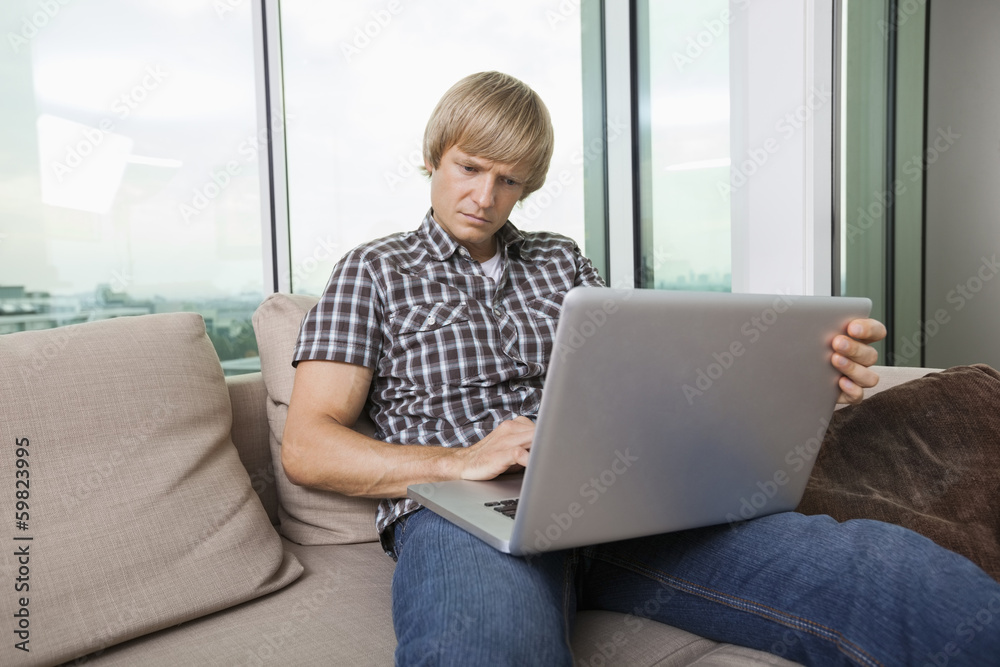 Serious mid-adult man using laptop on sofa at home Serious mid-adult man using laptop on sofa at home