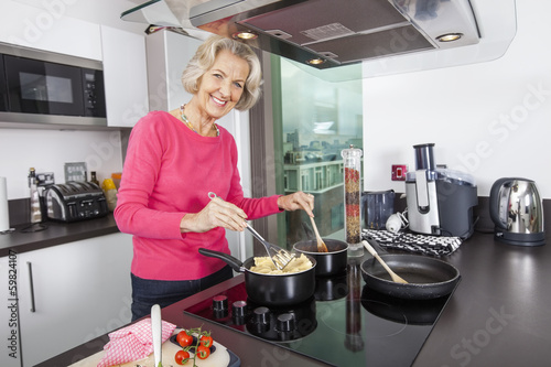 Portrait of happy senior woman cooking food at kitchen counter