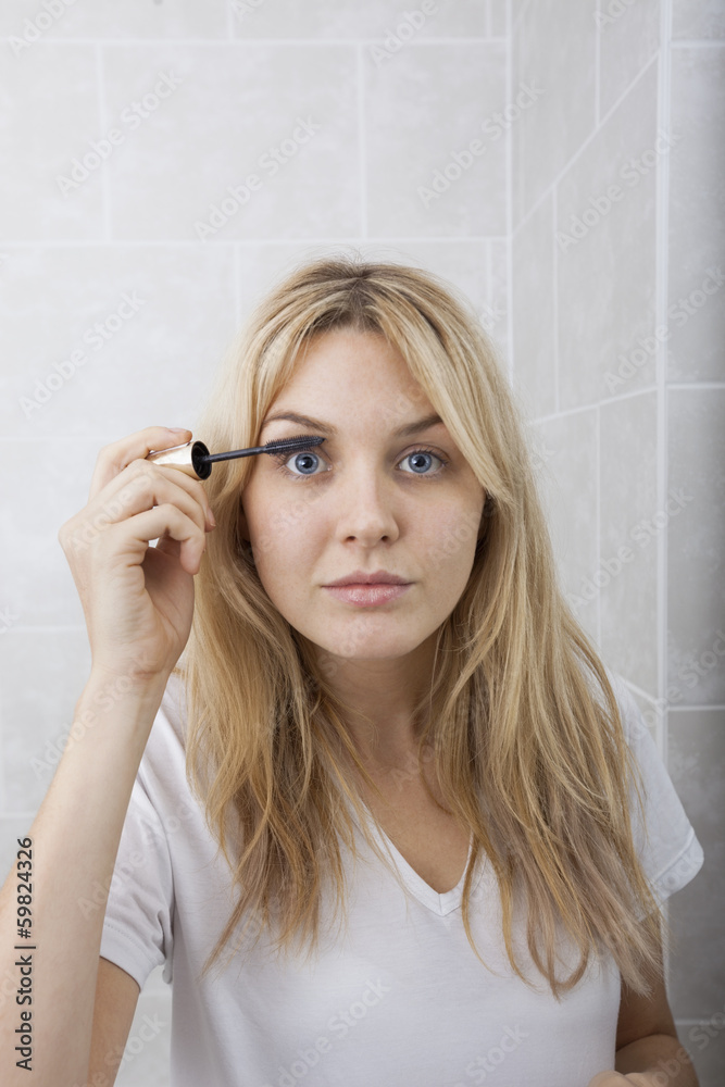 Portrait of young woman applying mascara in bathroom Portrait of young woman applying mascara in bathroom