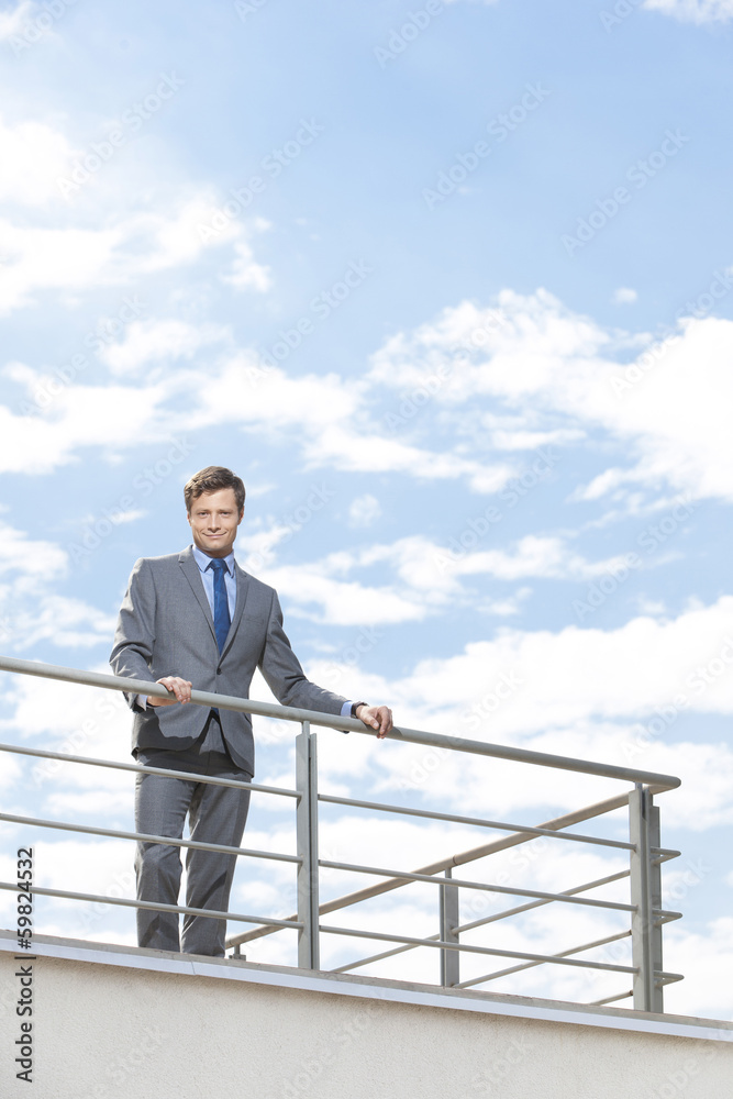Portrait of smiling businessman at terrace railings against sky