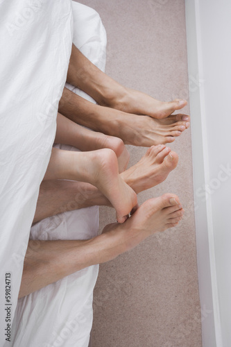 Low section of two men with woman in bed