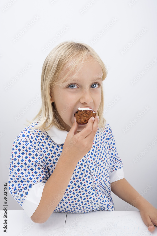 Portrait of cute girl eating muffin at table in house