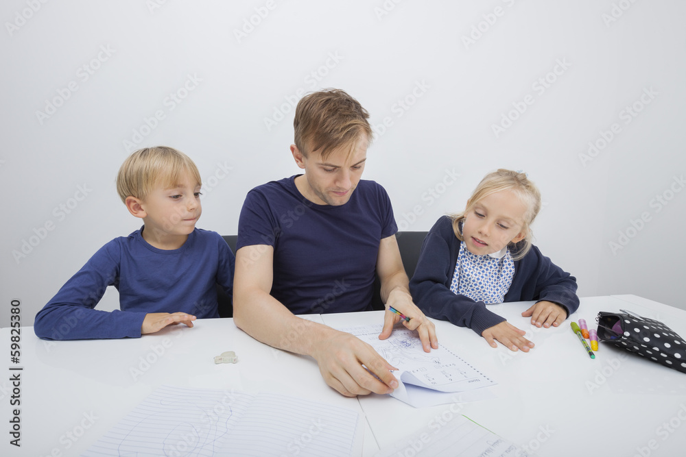 Father checking children's homework at table Father checking children's homework at table