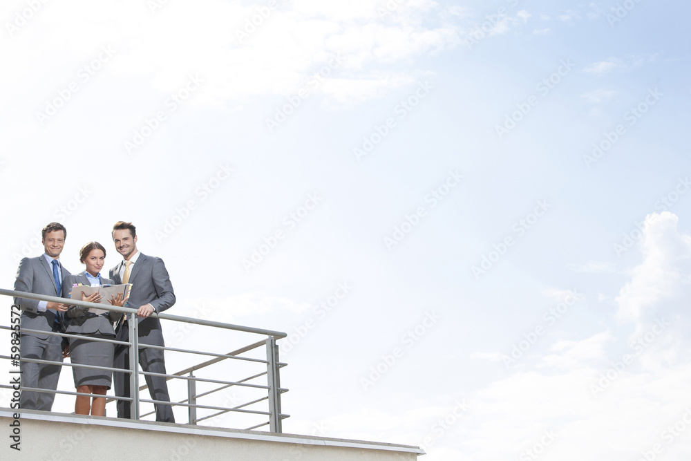 Businesspeople standing at terrace railings against sky Businesspeople standing at terrace railings against sky