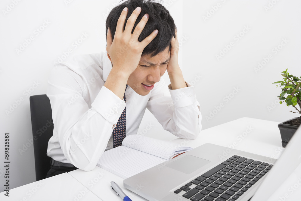 Frustrated businessman with head in hands sitting at desk in office Frustrated businessman with head in hands sitting at desk in office