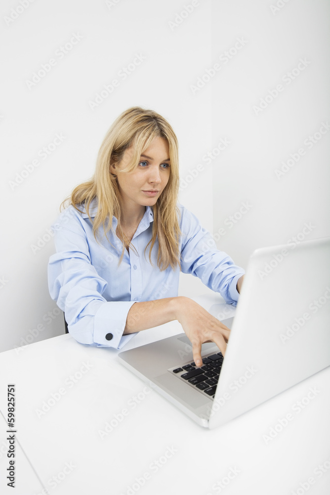 Beautiful young businesswoman using laptop at desk in office Beautiful young businesswoman using laptop at desk in office