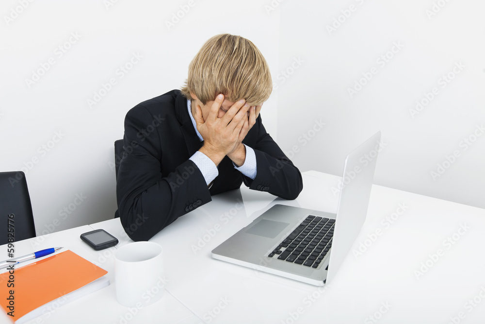Tired businessman with hands on face sitting at desk by laptop Tired businessman with hands on face sitting at desk by laptop