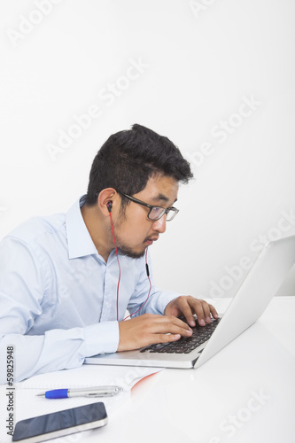 Concentrated businessman using laptop while listening music in office
