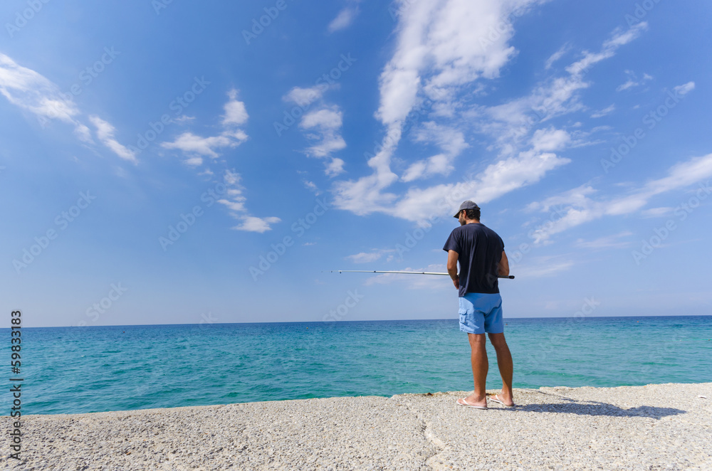 Man fishing on seaside horizon. Clear water and blue sky.