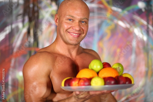 Muscular bald man with naked torso with plate of fruit photo