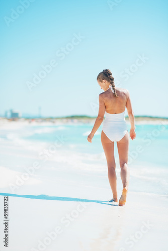 Young woman walking on sea shore. rear view