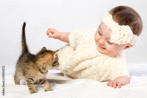 Smiling baby girl dressed in white fur plays with little kitten